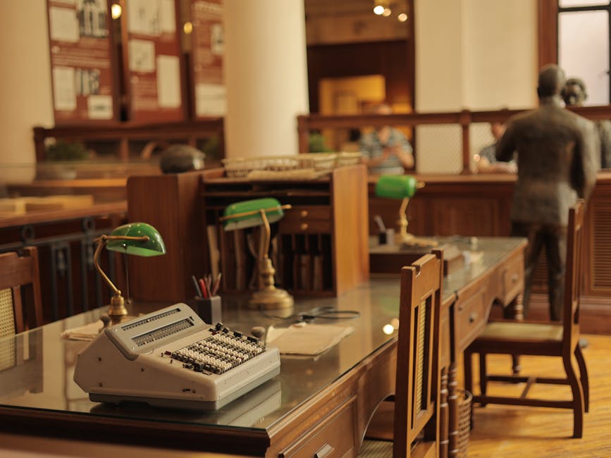 A classic office interior featuring a vintage typewriter, green desk lamps, and wooden furniture.