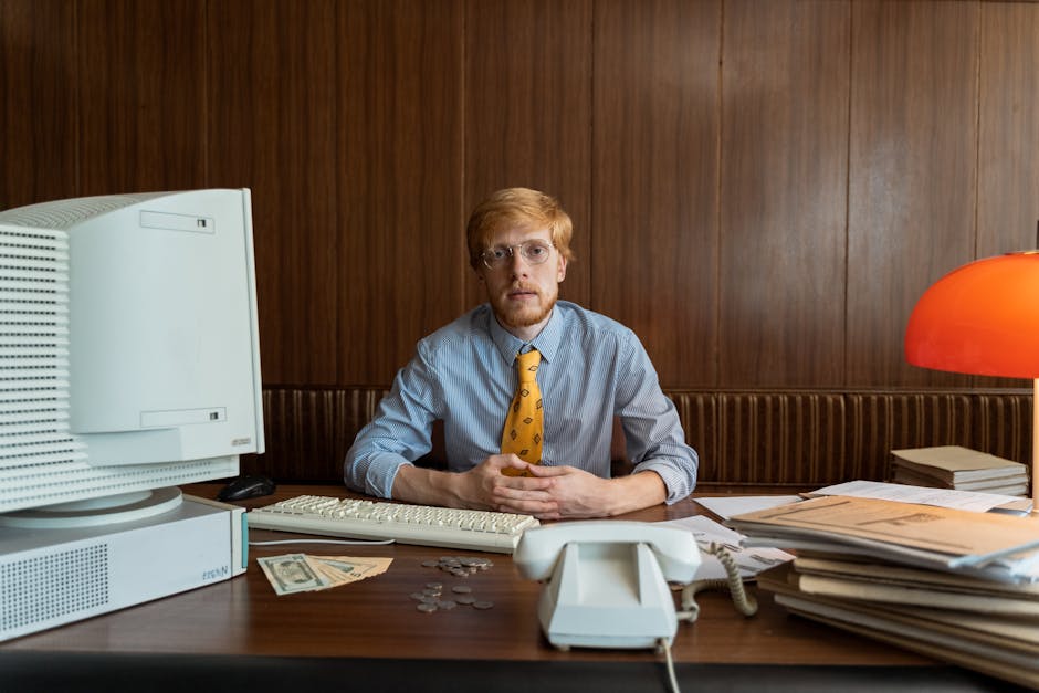Retro office scene with businessman in tie at desk, featuring vintage computer and files.