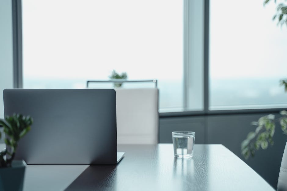 Minimalist office desk featuring a laptop and water glass in a modern business setting.